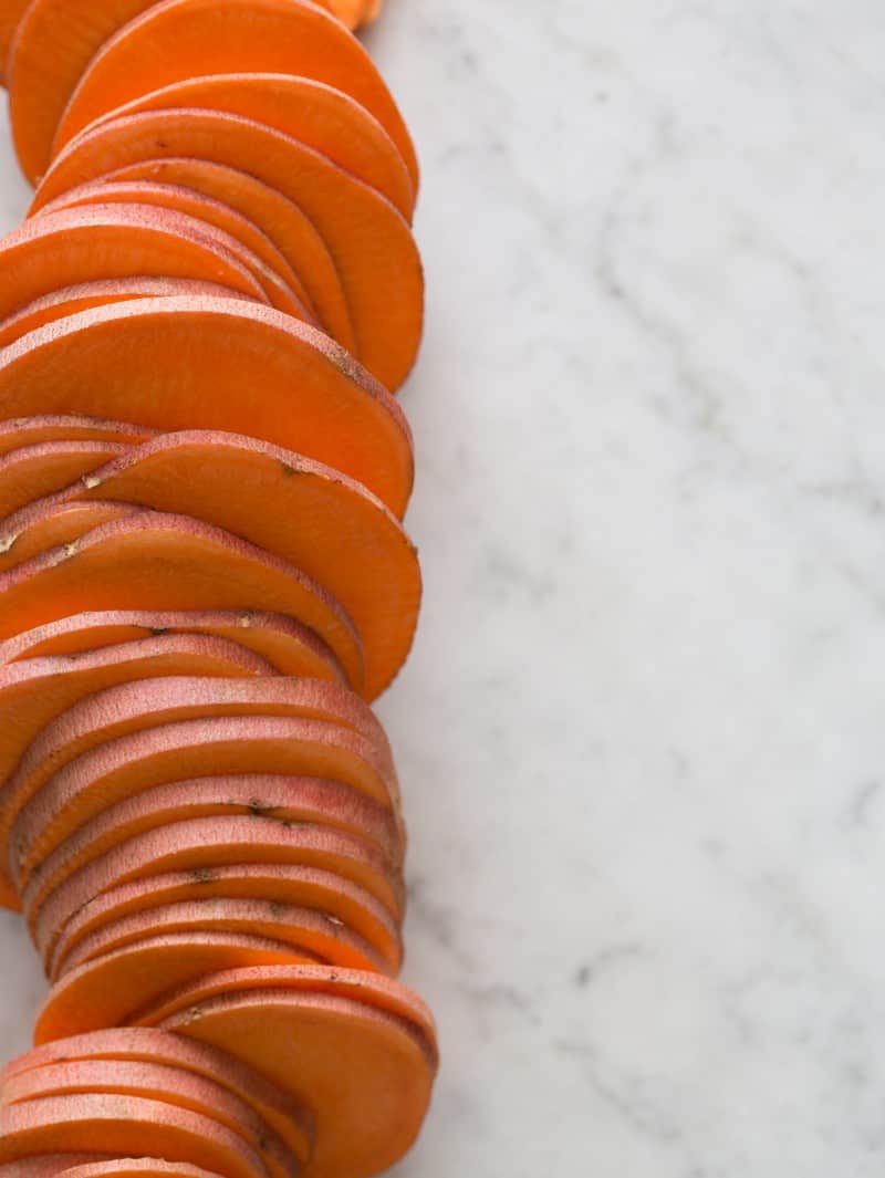 A sweet potato sliced into thin medallions, filed on a marble surface.