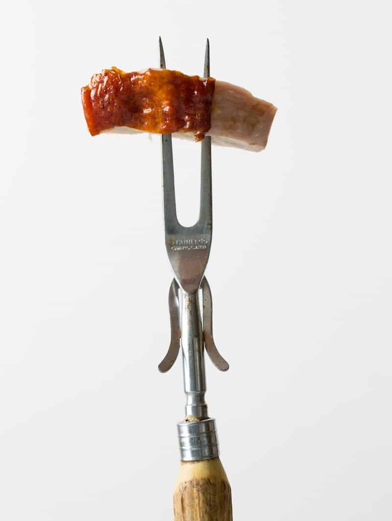 A close up of a piece of citrus and herb roasted turkey on a carving fork.