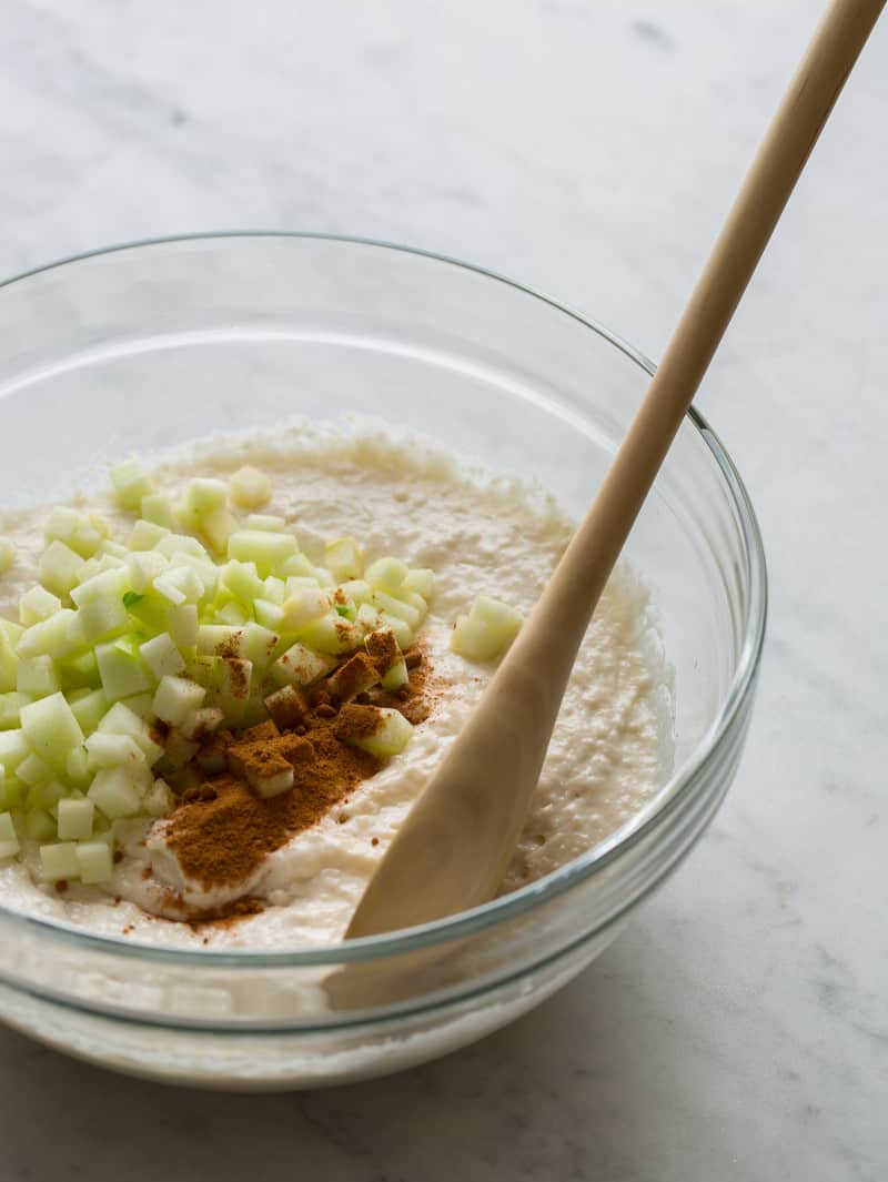 A bowl of apple cinnamon pancake batter ingredients with a wooden spoon.