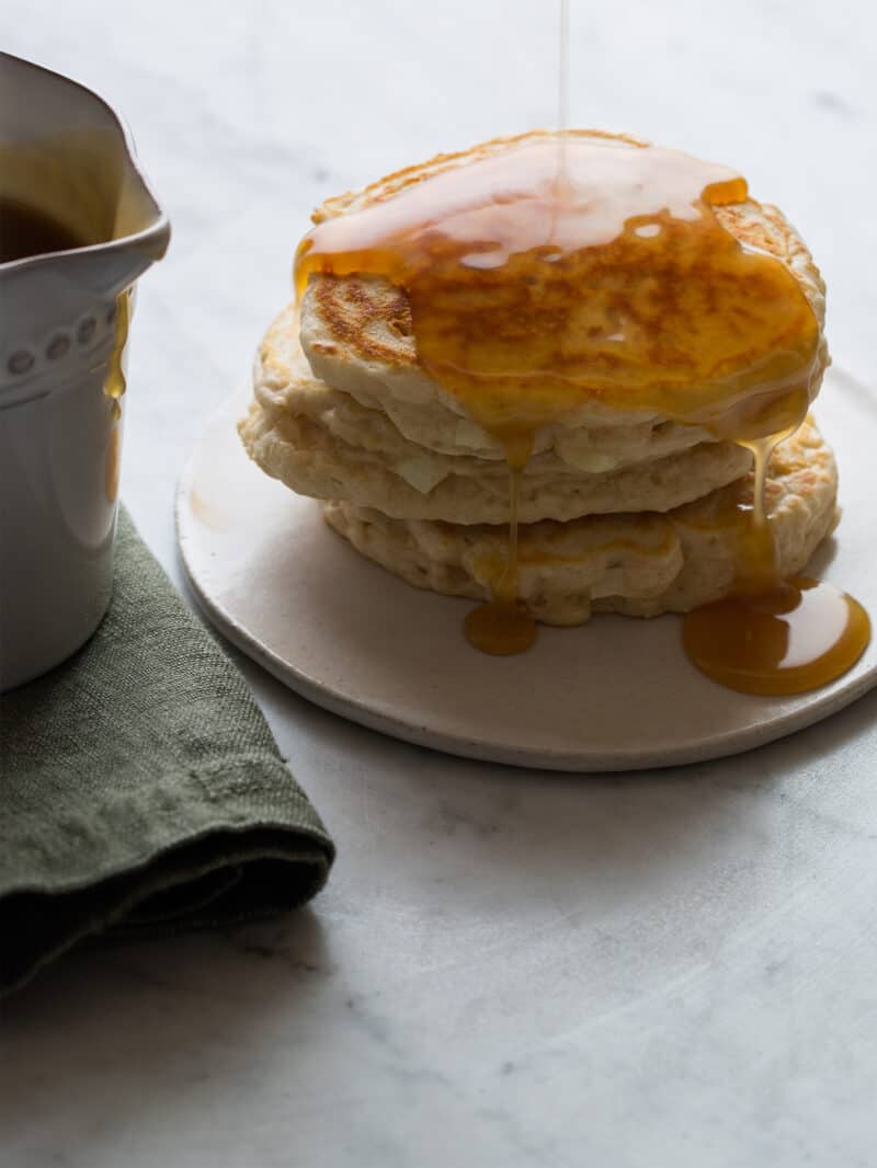 A stack of apple cinnamon pancakes with syrup on top and on the side.