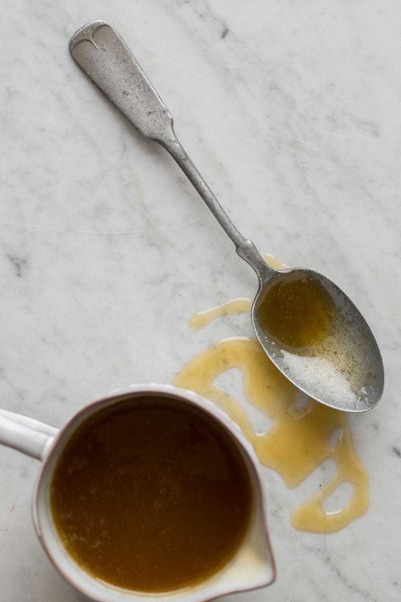 A cup of brown sugar buttermilk syrup next to a coated spoon.