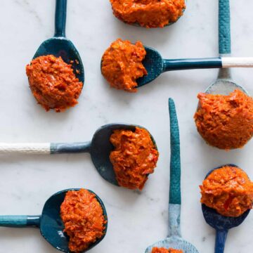 A close up of spoonfuls of harissa made two ways on several blue toned spoons.
