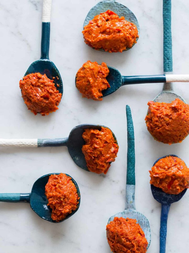 A close up of spoonfuls of harissa made two ways on several blue toned spoons.