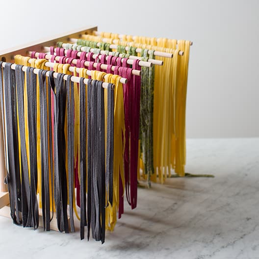 Multicolored homemade pasta hanging on pasta drying rack.