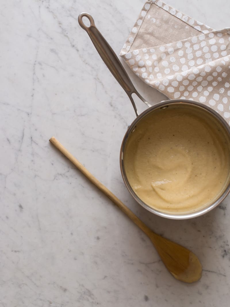 A pan of roasted cauliflower parsnip soup with linens and a wooden spoon.