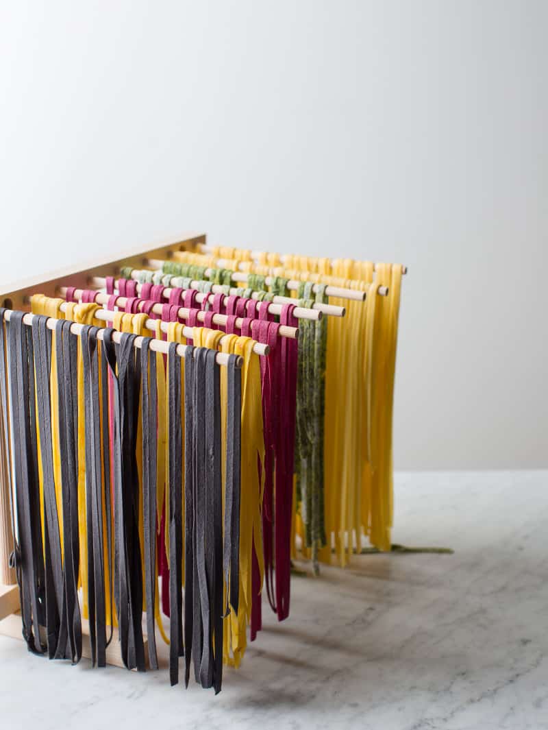 A variety of colorful pasta drying on a pasta rack.