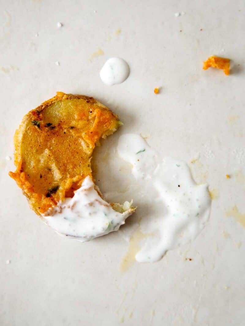 A chicken fried potato slice that has been dipped in ranch and a bite is taken out.