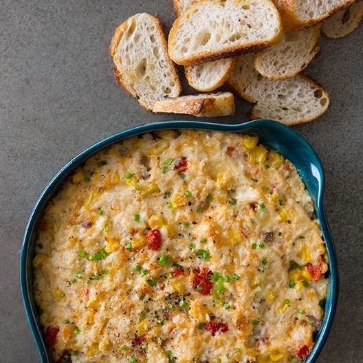 A baking dish full of hot crab dip with crostinis next to it. 
