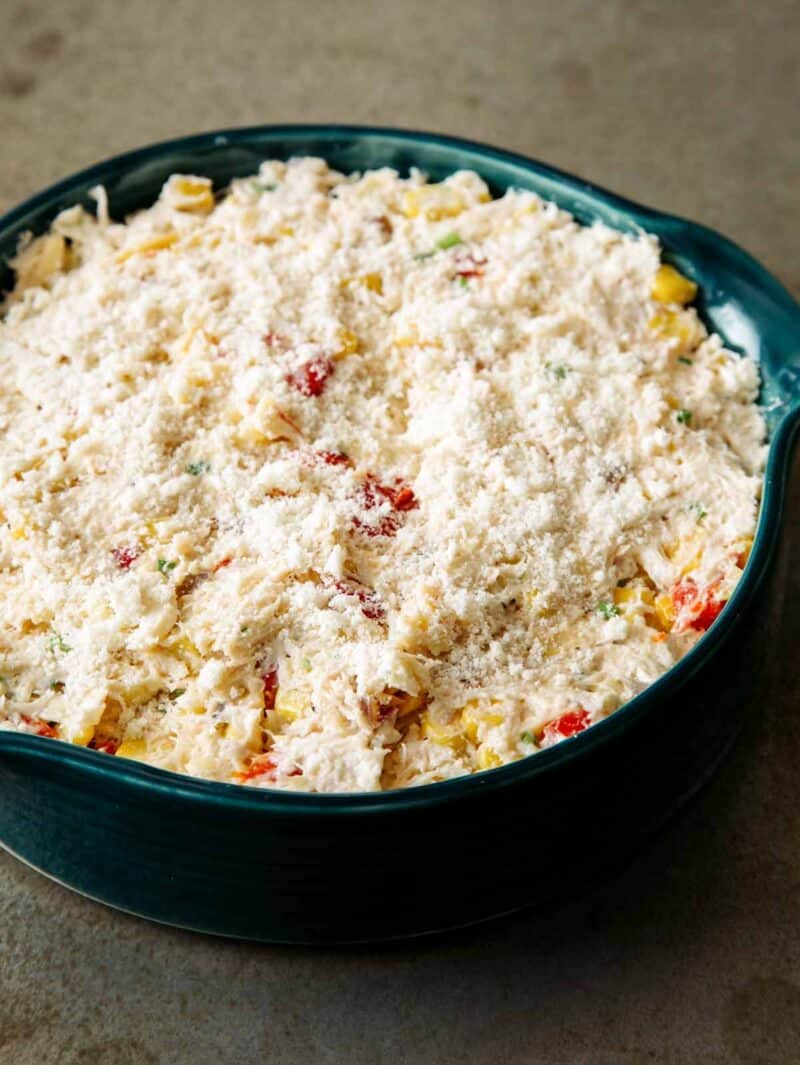 A close up of a dish of hot crab dip sprinkled with parmesan, ready to bake.