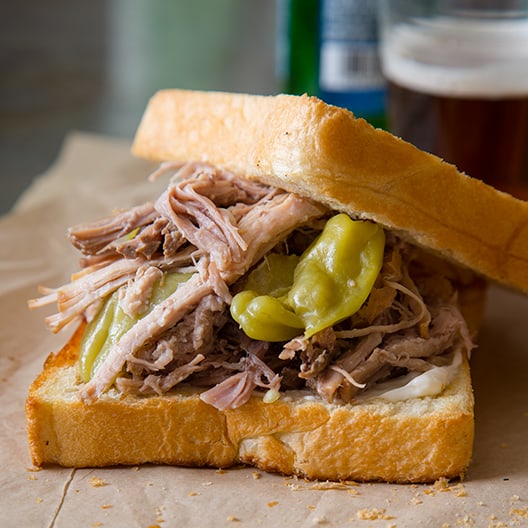 A close up of a slightly opened slow cooker pickled pulled pork sandwich.