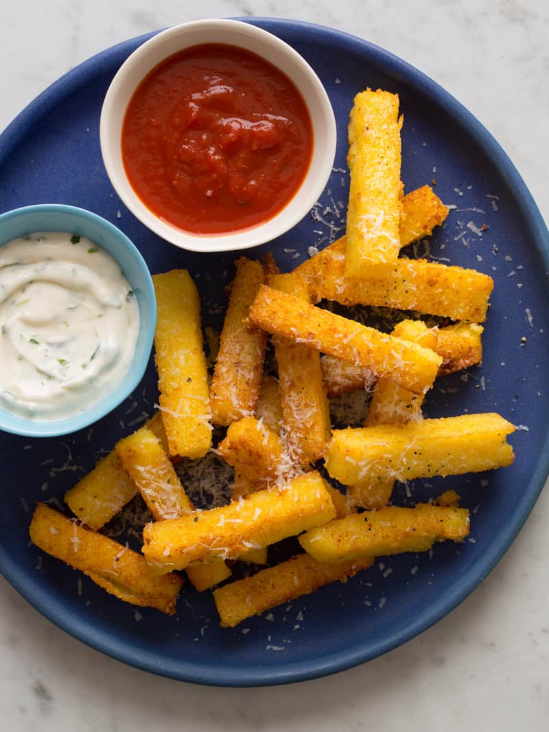 A close up of a plate of polenta fries with bowls of different sauces.