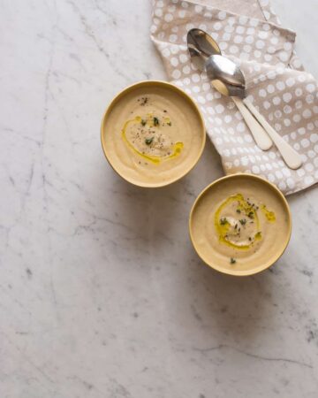 Roasted cauliflower parsnip soup in bowls next to napkins and spoons.