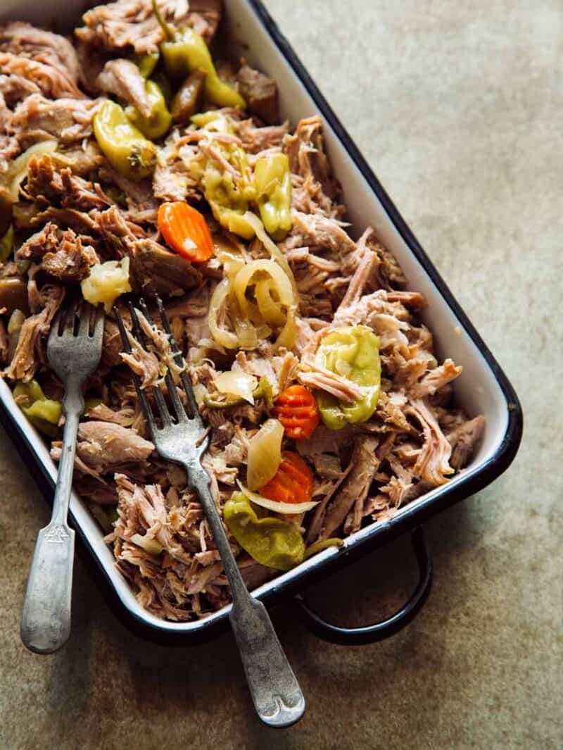 A dish is filled with slow cooker pickled pulled pork with forks.