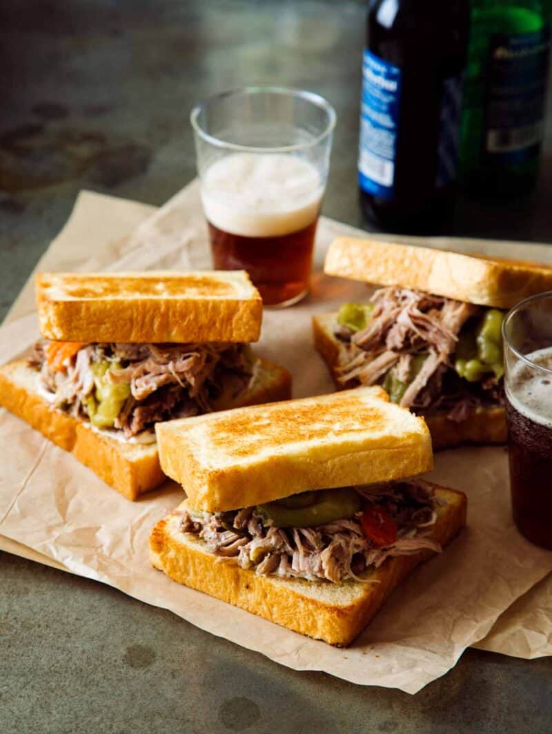 Several low cooker pickled pulled pork sandwiches on paper with beer.