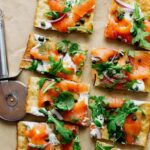 A sliced smoked salmon pizza with a pizza cutting wheel.