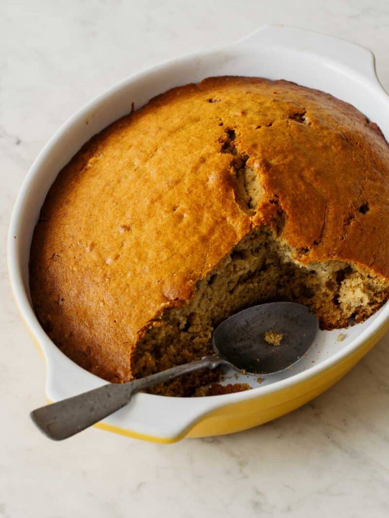 A close up of a whole chai banana cake with a piece taken out and a spoon.