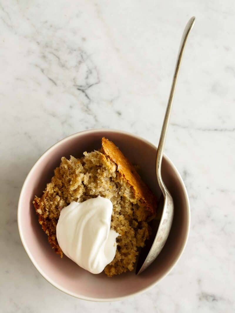 A bowl of chai banana cake with a dollop of whipped cream and a spoon.