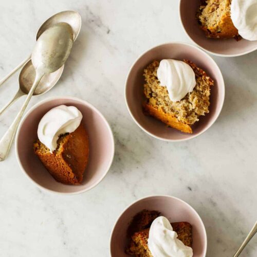 Bowls of chai banana cake with dollops of whipped cream and spoons on the side.