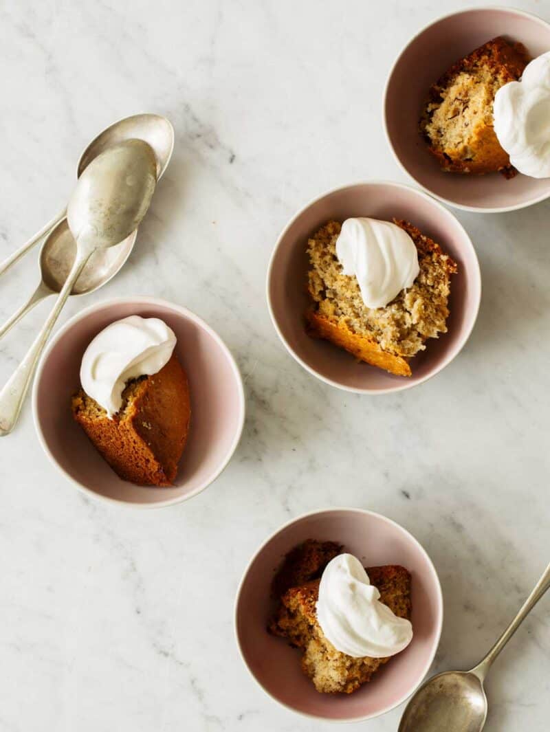 Bowls of chai banana cake with dollops of whipped cream and spoons on the side.