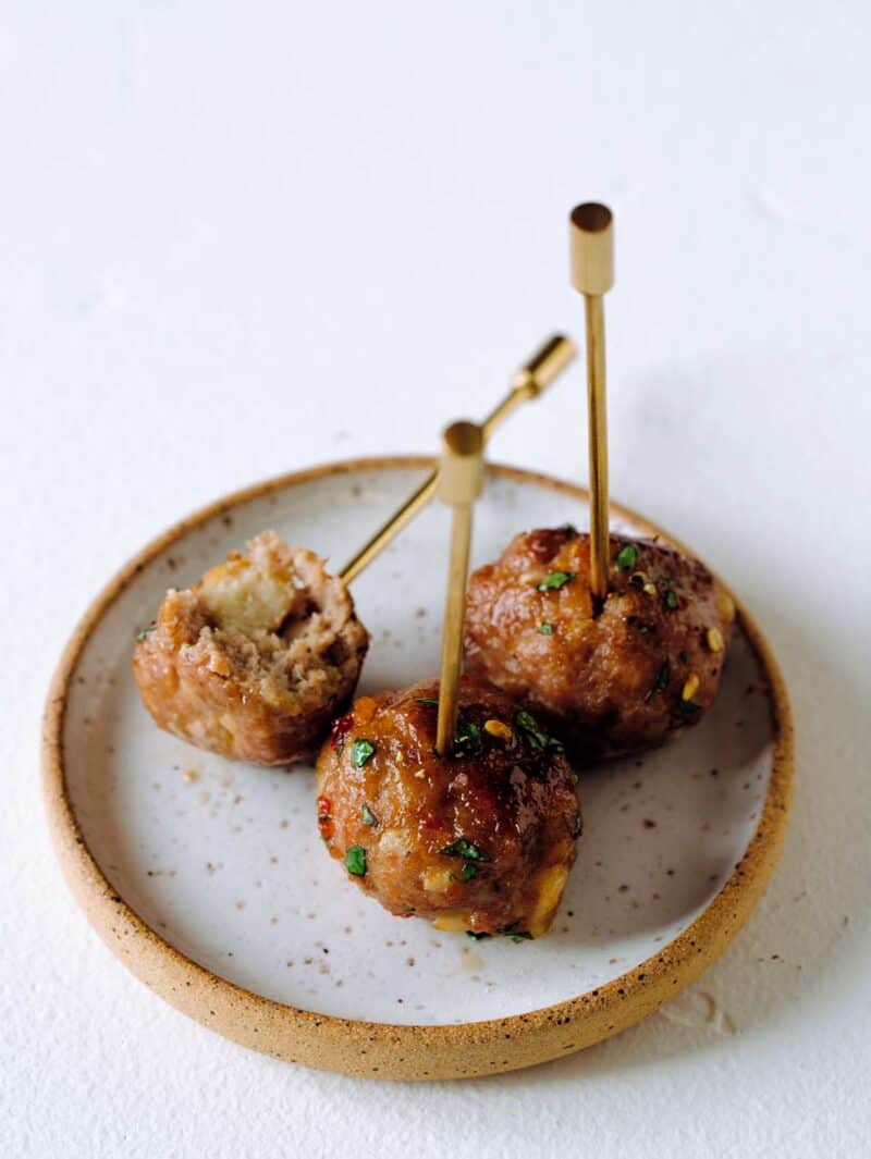 A close up of several ginger garlic cocktail meatballs with picks on a plate.