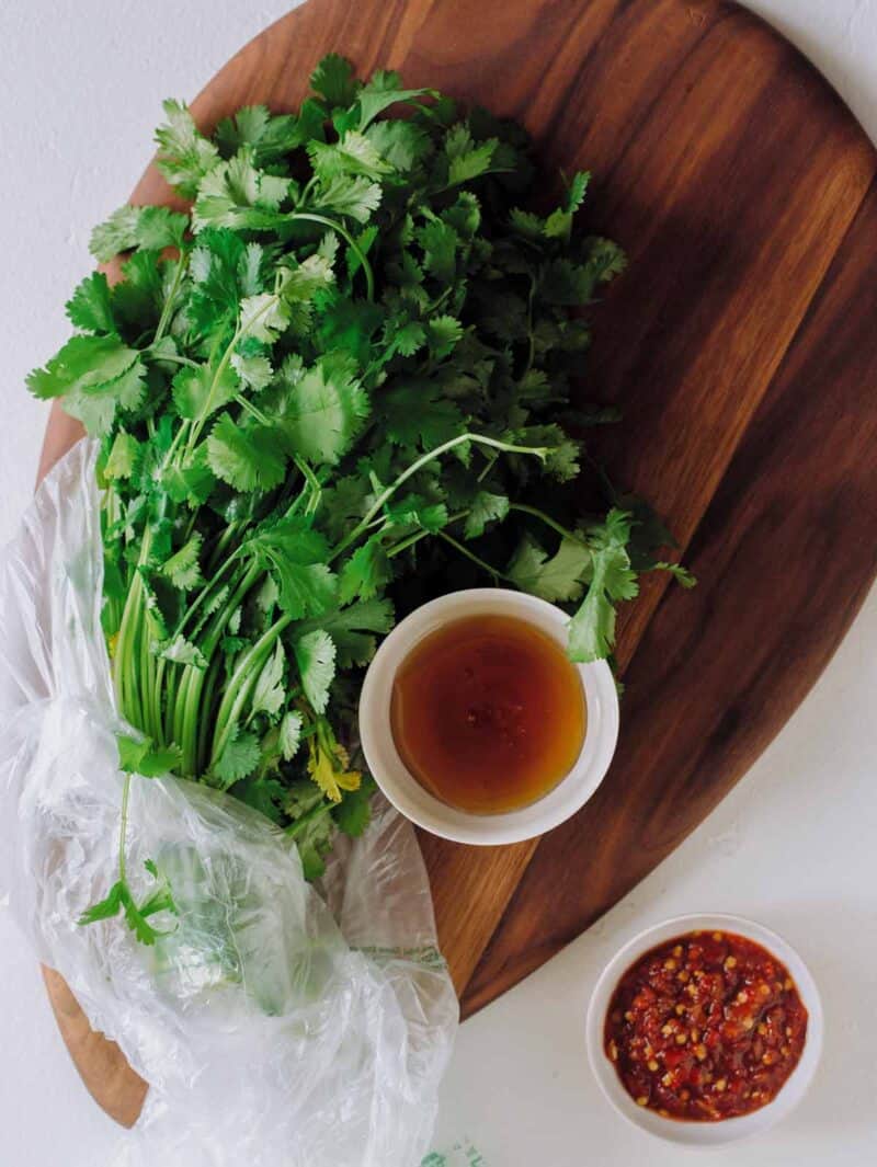 A bunch of cilantro and bowls of wet ingredients on a wooden cutting board.