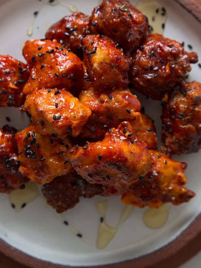 A close up of Korean chicken nuggets drizzled in honey and black sesame seeds.