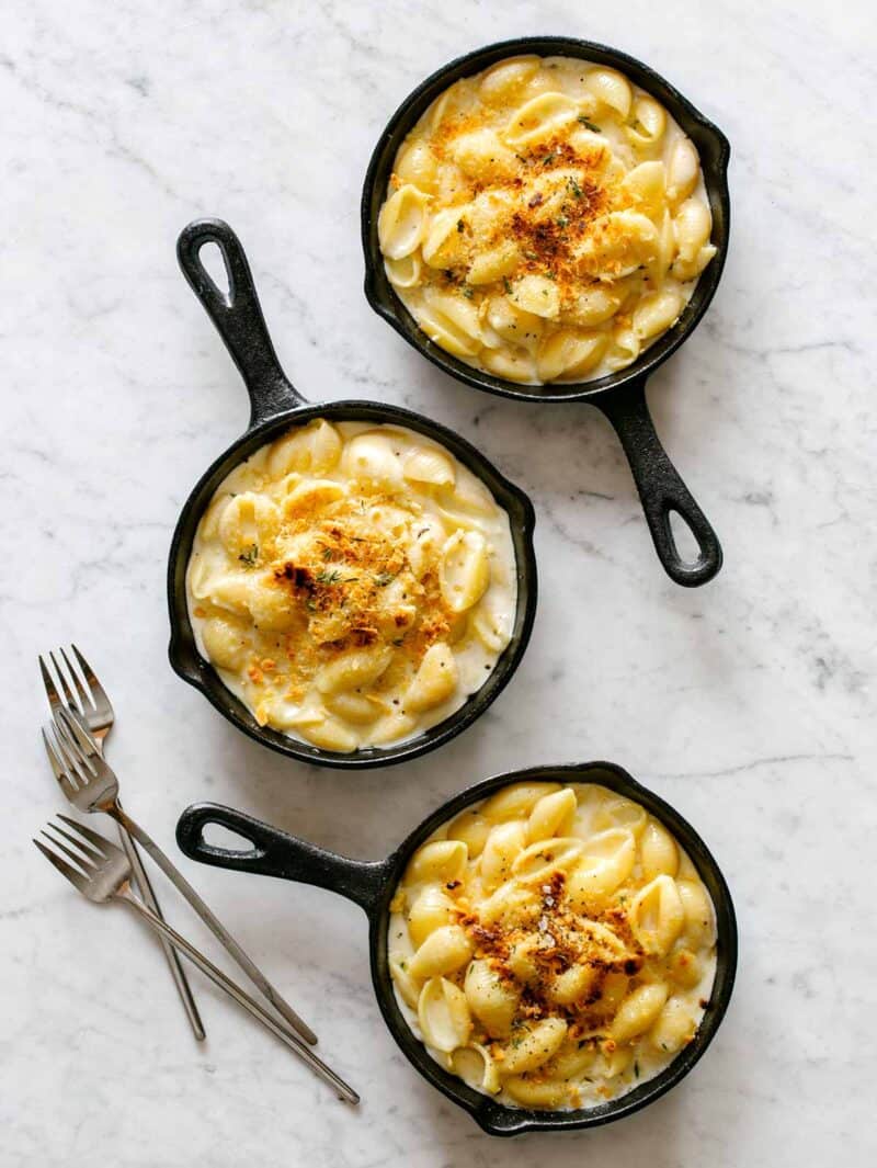 Several small cast iron skillets of creamy skillet mac and cheese with forks.