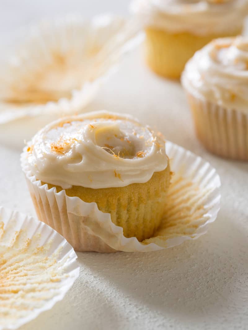 A close up of a butter cupcake with grapefruit buttercream half out of the cupcake wrapper.