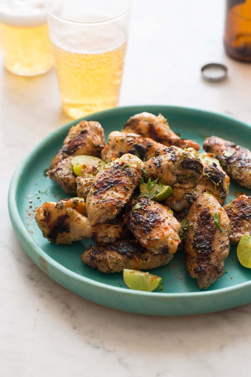 A plate of cilantro lime and yogurt grilled chicken wings with key lime wedges and drinks.
