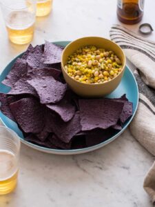 A plate of blue corn tortilla chips with a bowl of white bean and corn salsa.