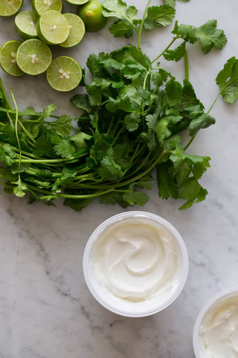 A close up of key lime halves, cilantro, and yogurt.