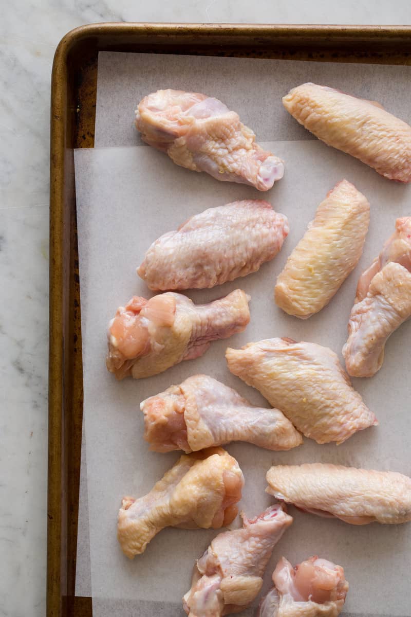 Raw chicken wings and drumettes on parchment paper on a sheet pan.