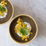 Bowls of spicy black bean soup garnished with sour cream, roasted corn, and cilantro.