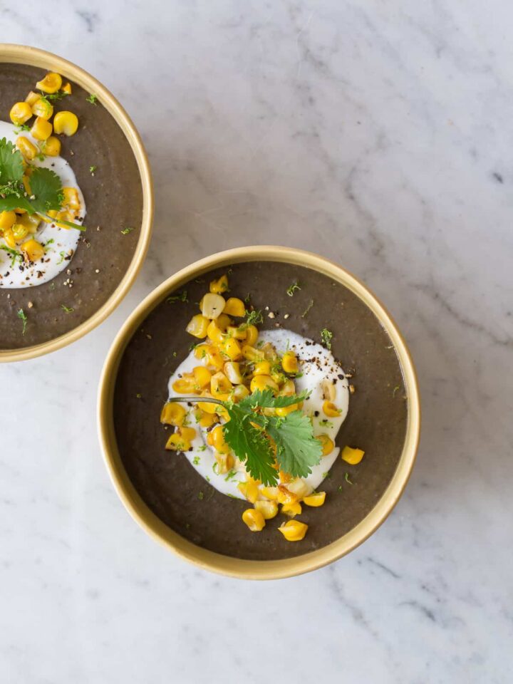 Bowls of spicy black bean soup garnished with sour cream, roasted corn, and cilantro.