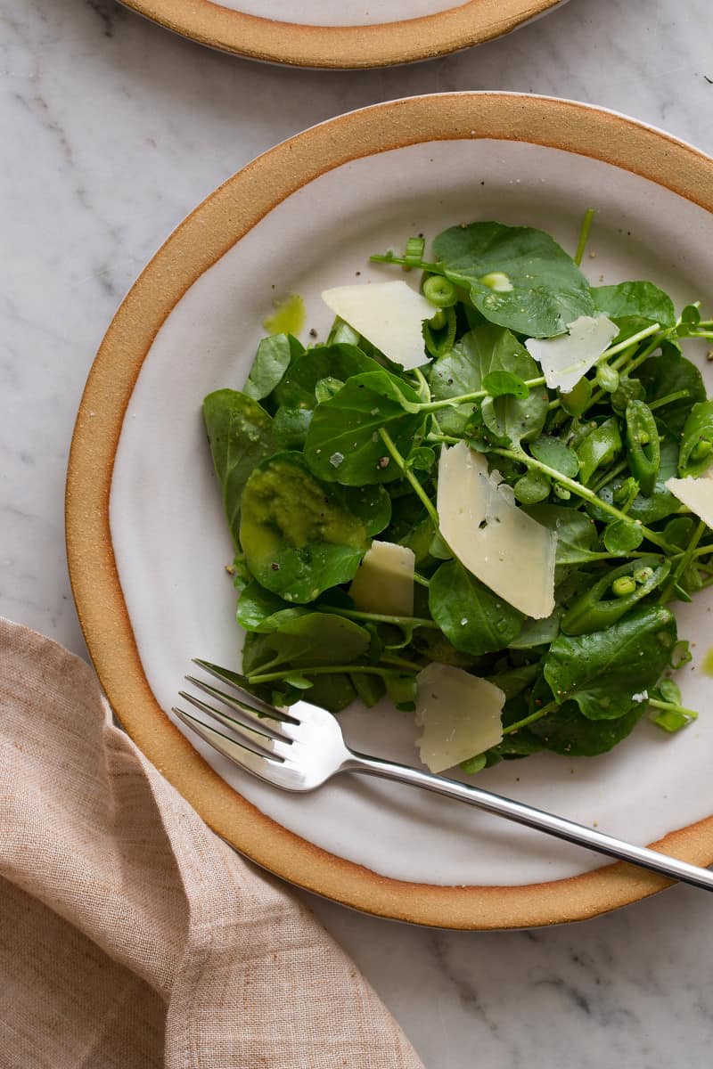 A close up of a plate of watercress salad with green apple vinaigrette and a fork.
