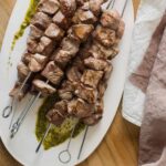 A plate of coconut milk marinated lamb kabobs with tarragon mint pesto and linens.
