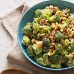 A bowl of broccoli crunch salad with a napkin and a wooden spoon.