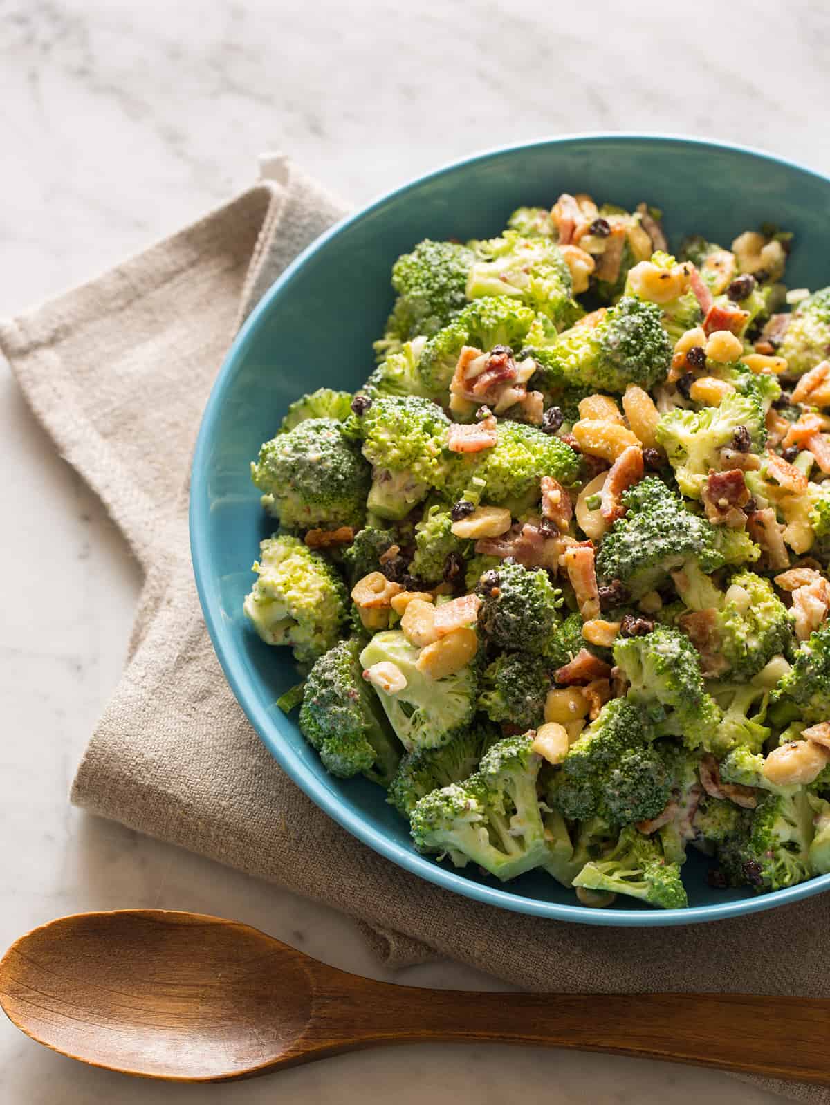 A bowl of broccoli crunch salad with a napkin and a wooden spoon.
