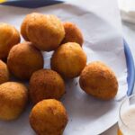 A close up of coxinha on a plate with a drink.