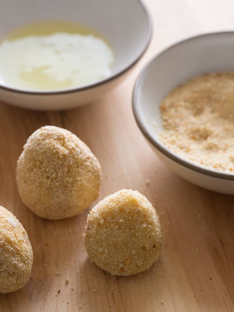 Prepped coxinha ready to be fried with bowls of egg and breadcrumbs.