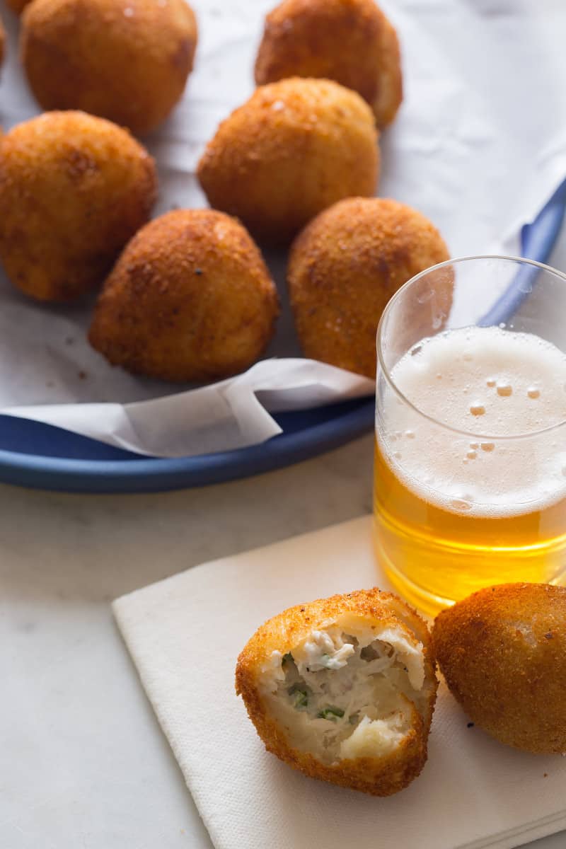 A close up of coxinha, some served and half eaten on a napkin with a drink.