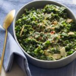 Creamed kale in a large serving dish with a spoon on a blue linen.