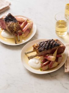 Plates of grilled rack of lamb with creamy feta horseradish sauce, roasted radishes, and drinks.