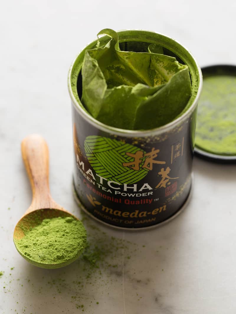 A close up of an open can of matcha powder with a wooden spoonful.