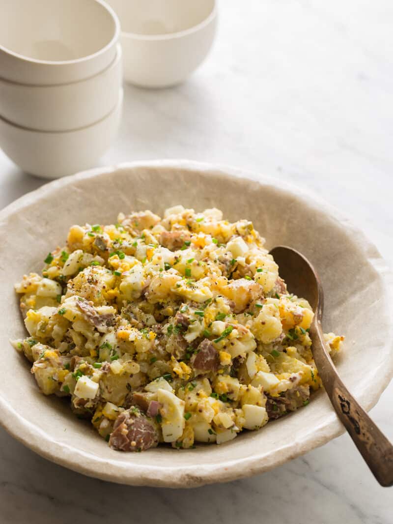 A close up of creamy potato salad in a bowl with a wooden spoon.