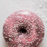 A close up of a chocolate and cardamom baked doughnut with sweet plum glaze and sprinkles.