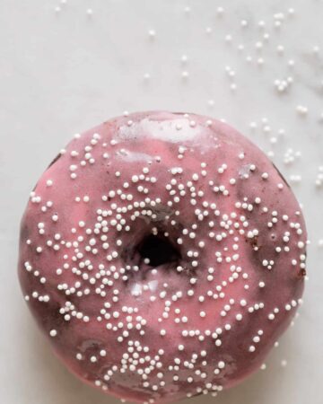 A close up of a chocolate and cardamom baked doughnut with sweet plum glaze and sprinkles.