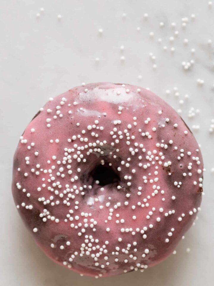 A close up of a chocolate and cardamom baked doughnut with sweet plum glaze and sprinkles.