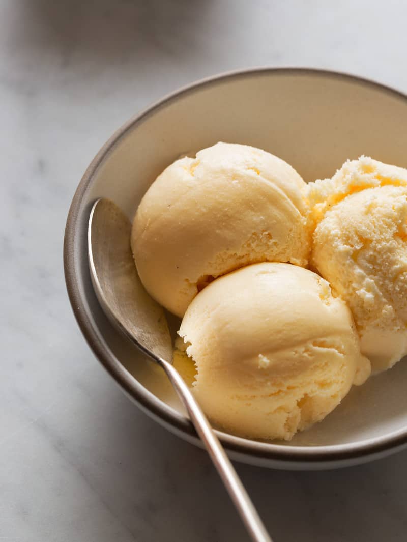 Ginger cantaloupe ice cream scoops in a bowl with a spoon in it.