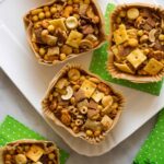 Wood and paper containers full of snack mix on a platter with green paper napkins.